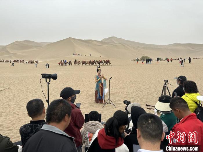 圖為2023年4月底，敦煌大漠“逐舞者”奧楠在鳴沙山月牙泉景區(qū)視頻直播，吸引游人圍觀?！●T志軍 攝